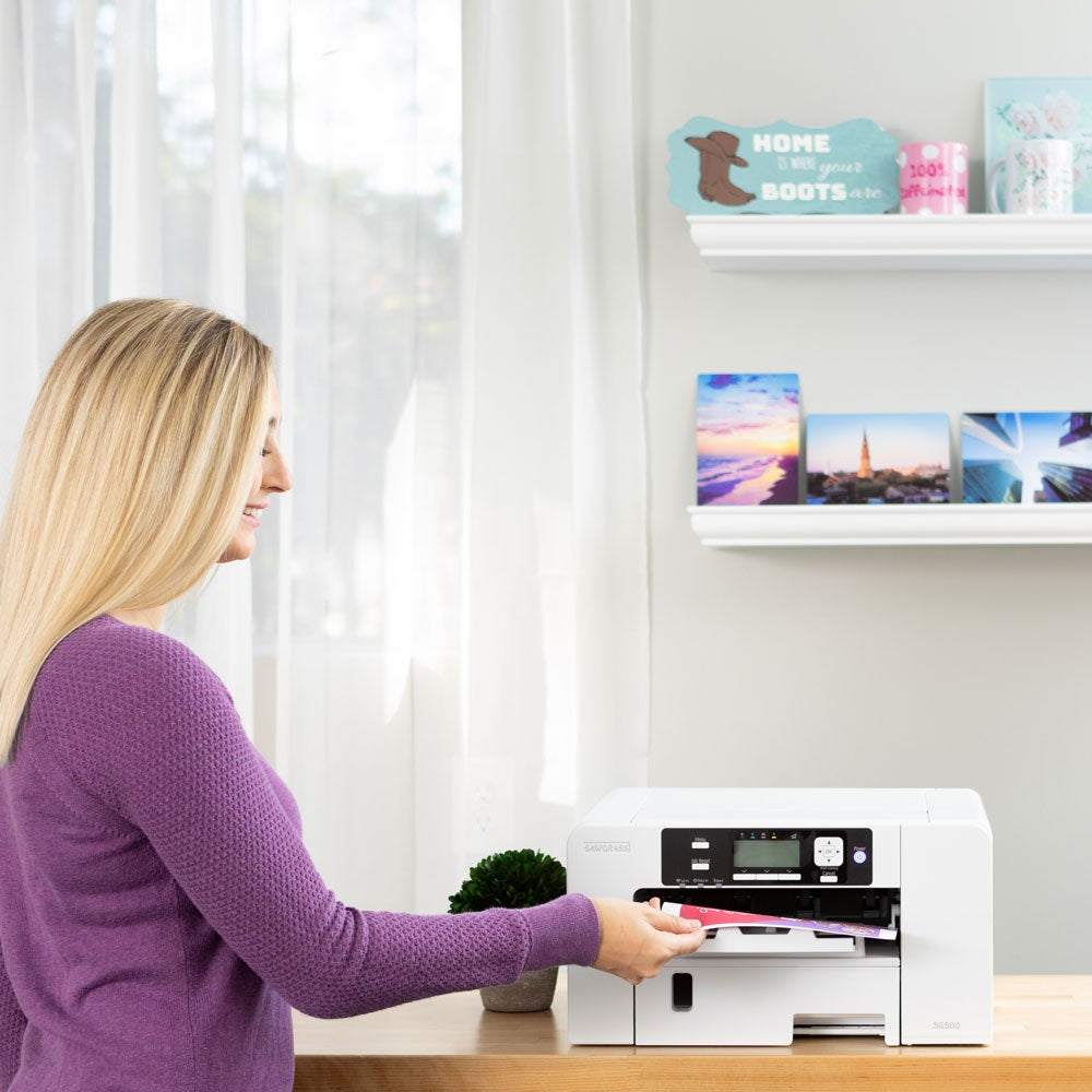 User operating the Sawgrass SG500 Sublimation Printer on a desk, bright indoor setting with decorative shelves.