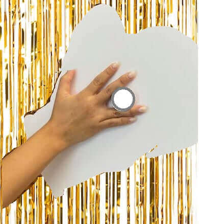 Hand holding a round photo booth prop against a shiny gold backdrop.