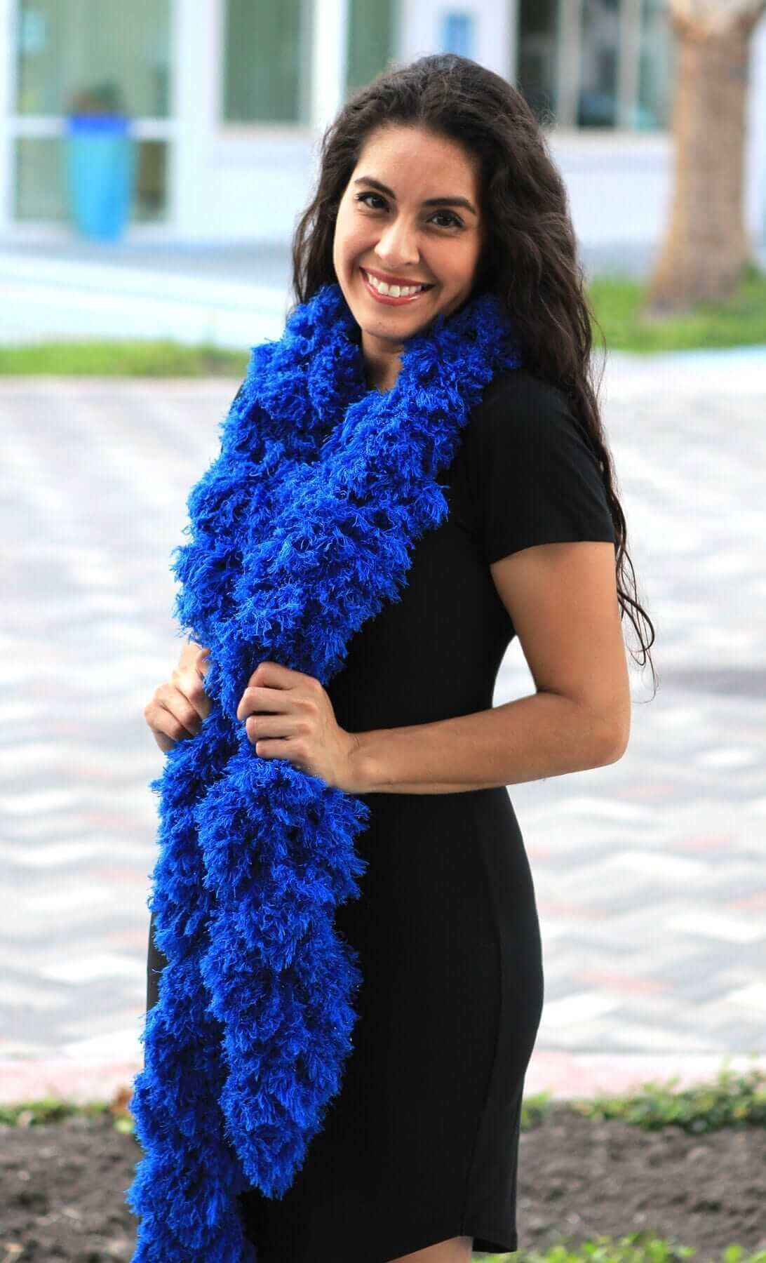 Smiling woman in a black dress wearing a super sized blue featherless boa, showcasing its vibrant color and soft texture.